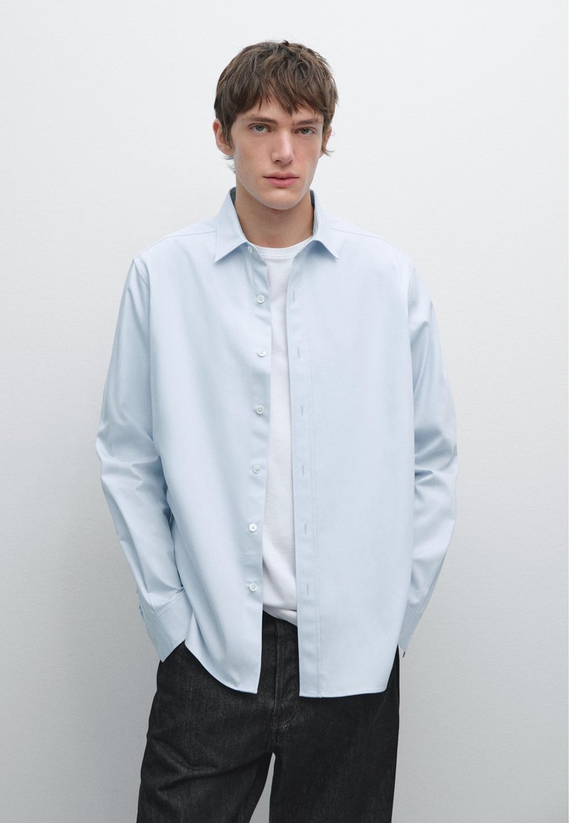 Camicia button-up azzurro chiaro realizzata in tessuto morbido, con maniche lunghe e vestibilità sartoriale, abbinata a pantaloni in denim scuri.