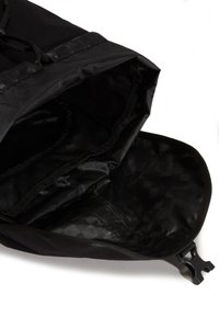 Zwarte stoffen rugzak met een openingen die de lege binnenkant toont, met een geblokte voering en een plastic zijklem op een witte achtergrond.