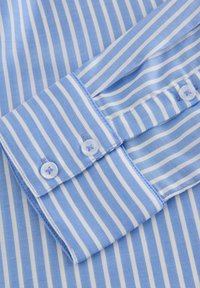 Lichtblauw-wit gestreepte overhemdkraag met knoopdetails, voorzien van een zachte katoenen textuur en contrasterende stiksels op de manchetten.