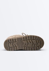 Zool van een beige winterlaars met diep profiel, merk “Oysho” en maat “37” zichtbaar op de zool, tegen een effen witte achtergrond.