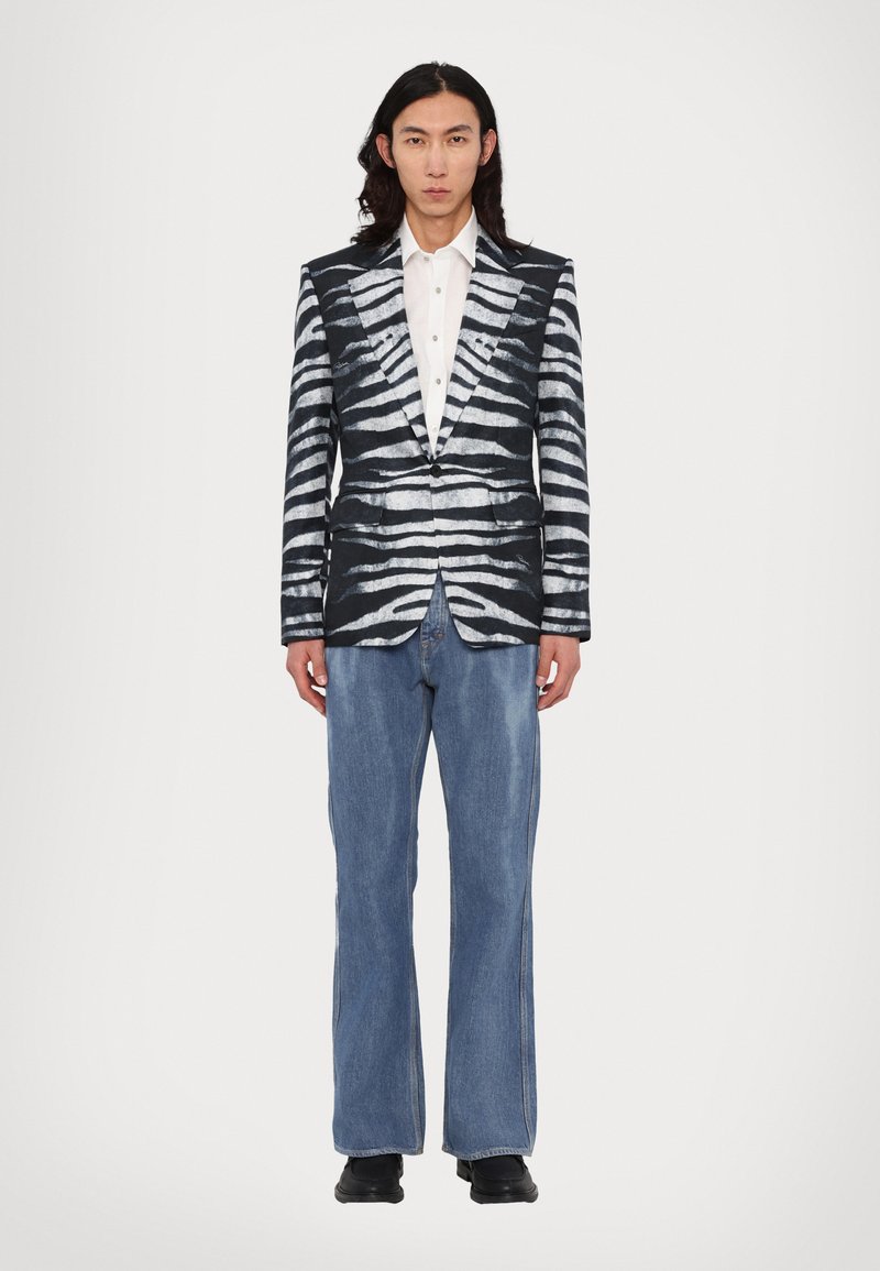 Sort og hvid stribet blazer med skarpe revers, parret med falmede blå denimbukser. Blazeren har en glat tekstur og en struktureret design.