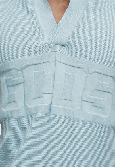 Ανοιχτό μπλε πλεκτό πουλόβερ με V-λαιμόκοψη και ανάγλυφα γράμματα «ECOOS» στο στήθος.