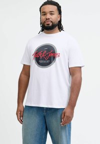 Valge puuvillane T-särk ümmarguse musta graafikaga, millel on punases kursiivis kirjutatud "Jack & Jones", all pool on trükitud "ESSENTIALS DEPT.".