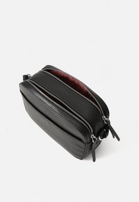 Borsa in pelle nera con superficie texture, due zip argentate e un interno foderato rosso a contrasto. Forma rettangolare e design slim.