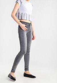 Šedý krátký top s volánkovými rukávy, doplněný šedými úzkými džínami. Obuv tvoří černé baleríny. Jednoduchý, přiléhavý střih.