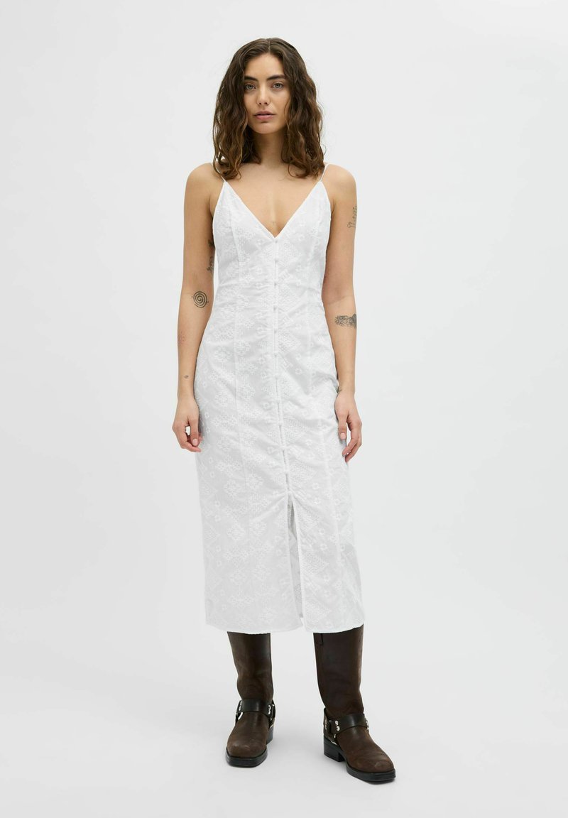 Vestido de algodón blanco con escote en V, tirantes ajustables, botones frontales y una abertura alta en el muslo, que presenta un sutil patrón geométrico.