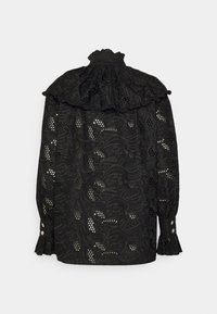 Blouse noire avec un col à volants, ornée d'une broderie florale complexe et de détails découpés. Poignets boutonnés et tissu texturé.