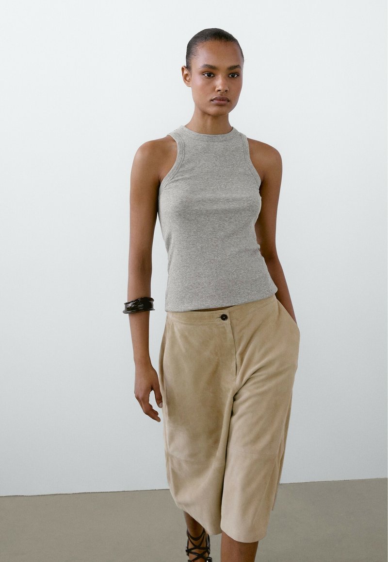Grijze geribbelde haltertop gecombineerd met beige suède culottes. Opmerkelijke details zijn een zijknopen sluiting en een enkellange snit.