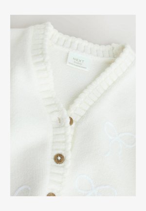 Cardigan per neonato bianco lavorato a maglia con colletto a costine, dotato di bottoni in legno e un delicato motivo a fiocchi. Realizzato in un morbido tessuto testurizzato.