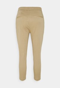 Pantalons stretch beige avec une texture lisse, dotés d'un design à jambes fuselées, d'une taille élastique et de deux poches arrière pour plus de fonctionnalité.