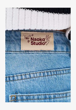 Dżinsy z denimu z beżową metką z napisem "Naoko Studio", na której znajduje się oko, gwiazdy i serce z liśćmi, przyszyte na tylnej części pasa.