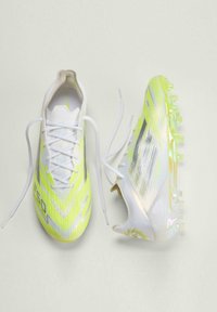 Ζευγάρι κίτρινων και λευκών ποδοσφαιρικών παπουτσιών, το ένα παρουσιάζει άνω όψη με κορδόνια, το άλλο γέρνει για να δείξει τις τάπες και το πλευρικό σχέδιο.