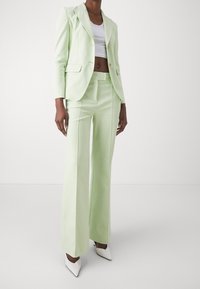 Completo su misura verde chiaro con giacca aderente a rever a punta, pantaloni larghi coordinati e décolleté bianche a punta.