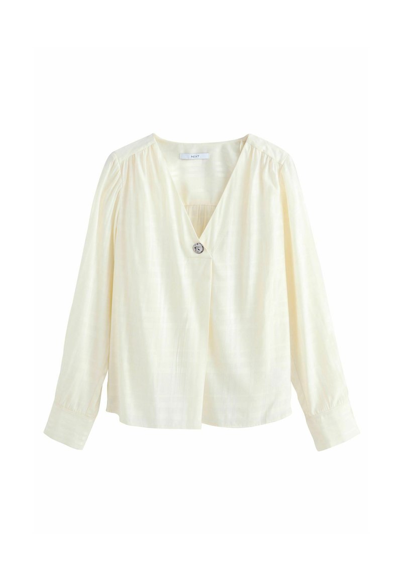 Blouse blanche à manches longues avec un col en V et un détail de bouton, présentant une texture subtile et des coutures d'épaule froncées pour un ajustement décontracté.