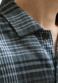 Camisa de cuadros gris y negro con cuello, cierre de botones y textura de tela suave con líneas finas y patrones contrastantes.
