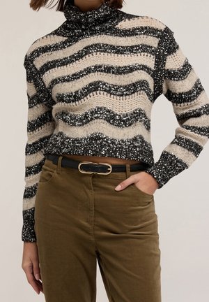 Persoon draagt een zwart-beige gestreepte gebreide coltrui, ingestopt in een bruine high-waisted broek met een zwarte riem en gouden gesp.