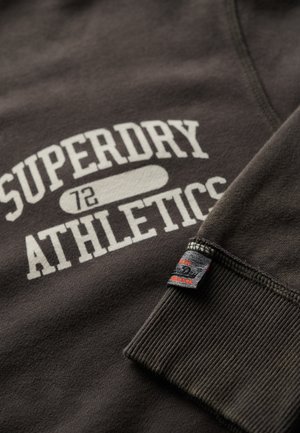 Ciemnoszara bluza z białym napisem "SUPERDRY ATHLETICS", ściągaczami przy mankietach oraz małą czarną metką z czerwonymi akcentami na rękawie.