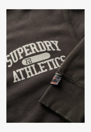Ciemnoszara bluza z białym napisem "SUPERDRY ATHLETICS", ściągaczami przy mankietach oraz małą czarną metką z czerwonymi akcentami na rękawie.
