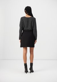 Blouse noire à manches longues avec des taches blanches, associée à une jupe noire. Présente un décolleté rond et des bottines avec zippers à l'arrière.
