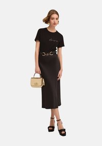Camiseta negra con el texto "Haz que hoy sea increíble", combinada con una fluida falda midi negra, un cinturón de herrajes dorados y un bolso dorado metálico. Sandalias de plataforma negras.