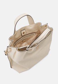 Beżowa torba na ramię z teksturą, złotymi okuciami, wewnętrzną kieszenią na zamek oraz podszewką z nadrukiem. Otwarty fason z podwójnymi uchwytami dla łatwego dostępu.