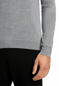 Grauer Langarmpullover aus einem weichen, strukturierten Stoff, mit einem gerippten Bund und Saum, kombiniert mit schwarzen, eng anliegenden Hosen.
