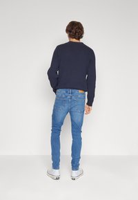 Suéter de canalé azul marino combinado con jeans ajustados de mezclilla azul claro. Los jeans cuentan con bolsillos traseros y un parche de cuero en la cintura. Zapatillas blancas.