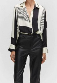 Czarna i biała bluzka w paski wykonana z gładkiego materiału, z kołnierzykiem, zapięciem na guziki z przodu i długimi rękawami, zestawiona z spodniami z czarnej sztucznej skóry.