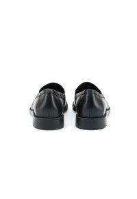 Mocassins en cuir noir à finition lisse, forme arrondie et détails de couture minimalistes. La semelle est plate et légèrement texturée.