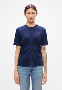 T-shirt in cotone blu navy a maniche corte con scollatura a girocollo e logo ricamato sul davanti. Texture liscia con dettaglio di arricciatura laterale.