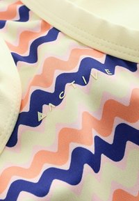 Tissu à rayures ondulées colorées en pêche, bleu marine, vert clair et rose, avec le mot « ACTIVE » en lettres en relief près d’une bordure beige.