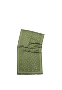 Bufanda verde con un diseño de patrones, con bordes con flecos, que presenta un diseño abstracto repetido. El material parece suave y tiene una textura lisa.