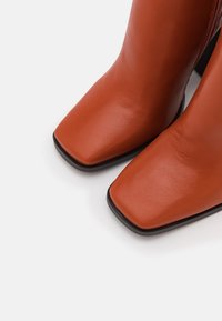 Bottines en cuir marron à bout carré, design épuré, texture lisse et petit talon noir, incarnant un style minimaliste et élégant.