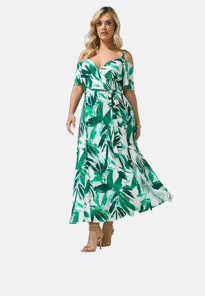 Frau, die ein grün-weißes Maxikleid mit schulterfreien Ärmeln, einem Wickelbund und beigen Sandalen mit hohen Absätzen trägt.