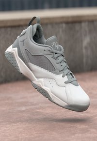 Adidași albi și gri cu accente din plasă, design aerodinamic, partea superioară texturată și talpă din cauciuc cu modele circulare pentru aderență.