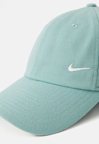 Light teal cap with a structured design, made of textured fabric. Features a white embroidered Nike logo on the front.