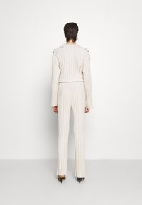 Krémově bílý žebrovaný pletený set, který se skládá z přiléhavého topu s dlouhým rukávem a upravených kalhot s lichotivou siluetou a jemnými texturovými detaily.