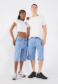 Denim shorts in light blue, loose fit, with front pockets. White fitted t-shirt and shoes with mixed colors on models against a plain background.