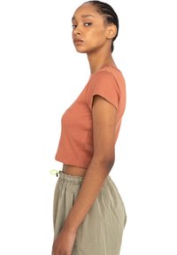 Camiseta corta de color óxido con mangas cortas, hecha de una tela texturizada. Combinada con pantalones de cintura elástica de cuadros claros con cordón.