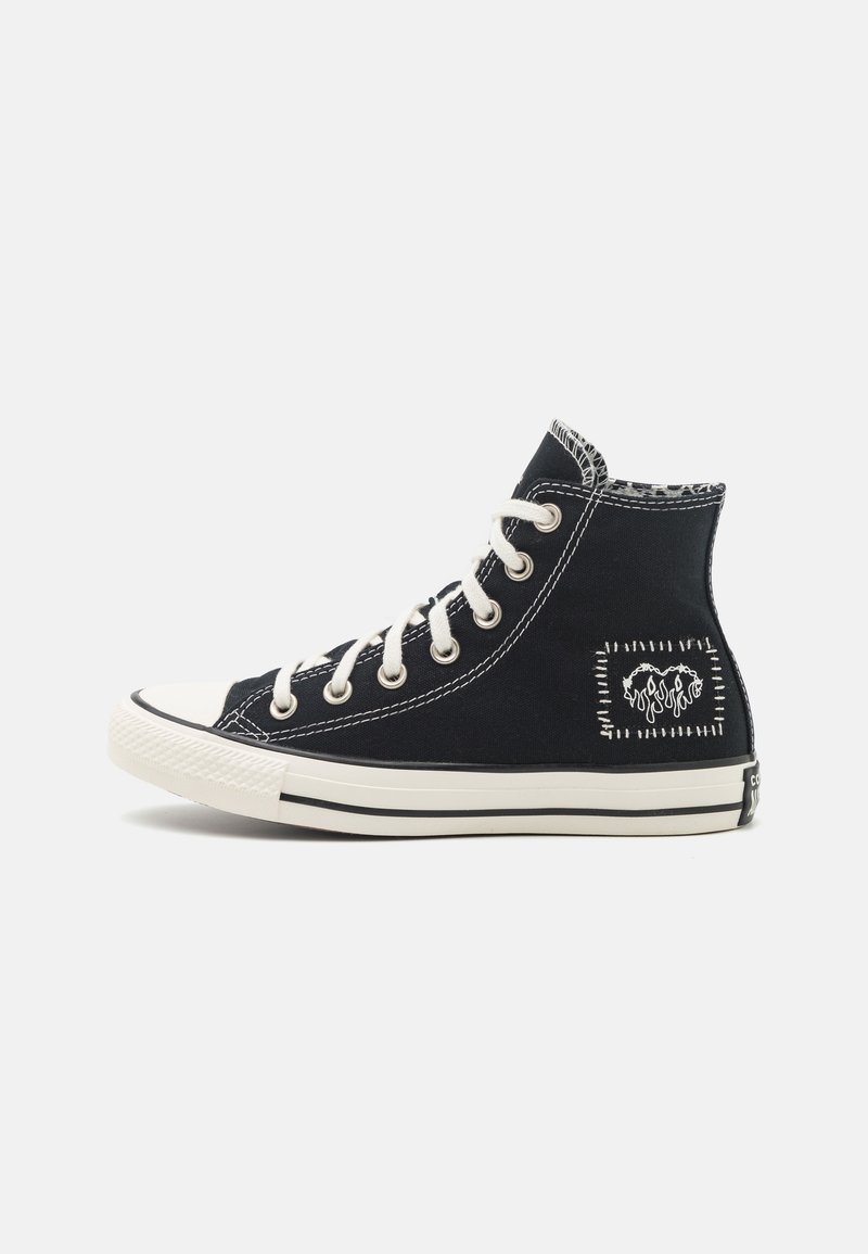 Zapatillas altas negras con suelas de goma blanca, con costuras blancas y un logo bordado en el lateral. Material de lona.