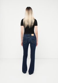 Dark blue flared jeans with a classic five-pocket design and subtle stitching details. Back features a leather patch above the right pocket.