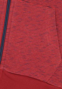 Rood en marineblauw gestreepte stof, met een ritszak en geribbelde zoom. De textuur is zacht, met opvallende strepen en een consistent patroon.