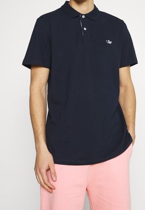 Polo bleu marine en coton, avec col, manches courtes, patte de boutonnage à trois boutons et petit logo blanc en forme de bateau sur la poitrine.