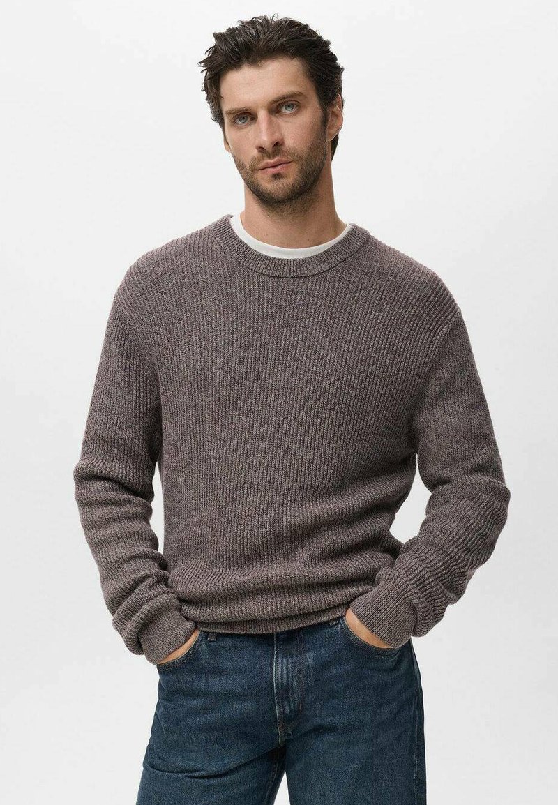 Suéter de punto acanalado para hombre en un tono púrpura suave, con cuello redondo y mangas largas, combinado con jeans de mezclilla oscuros.