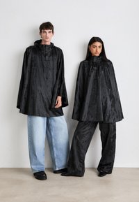 Sorte satengponchoer med hette, med en løs passform og subtil glans. Kombinert med vide jeans og svarte bukser. Minimalistisk design.