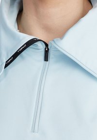 Jasnoniebieska sportowa kurtka z suwakiem do szyi, z czarnym uchwytem suwaka i czarnym sznurkiem z białym napisem "O'Neill".