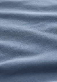 Mīksta gaiši zila auduma ar smalku tekstūru un maigām locījumiem, kas rada vieglu ēnu un dziļumu.