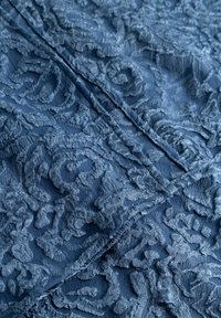 Navy blue textured fabric featuring intricate floral lace patterns with a slightly raised thread, creating depth and contrast.