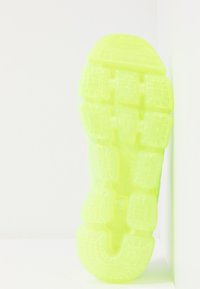 Neon žlutá podrážka tenisky s texturovaným vzorem a několika gripovými sekcemi, s zakřiveným tvarem a hladkými okraji.