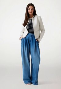 Veste ajustée de couleur claire avec boutons décoratifs, associée à un pantalon en denim bleu ample et taille haute. Haut rayé bleu marine et blanc en dessous.